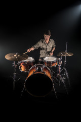 Professional drummer playing on drum set on stage on the black background