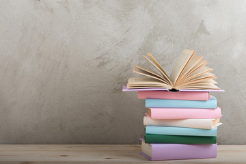 Education and reading concept - group of colorful books on the wooden table, concrete wall blackboard