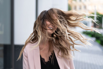 long wavy hair flying in the wind. Very beautiful young girl in a great mood on the street in good...