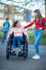 Teenage Girl In Wheelchair Talking With Friend As They Leave High School