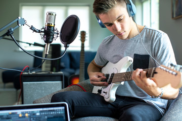 Teenage Boy Playing Guitar And Recording Music At Home