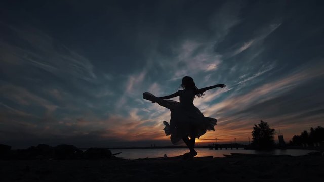 silhouette of a girl circling in a flying dress at sunset. Ballerina dancing gracefully on the beach.