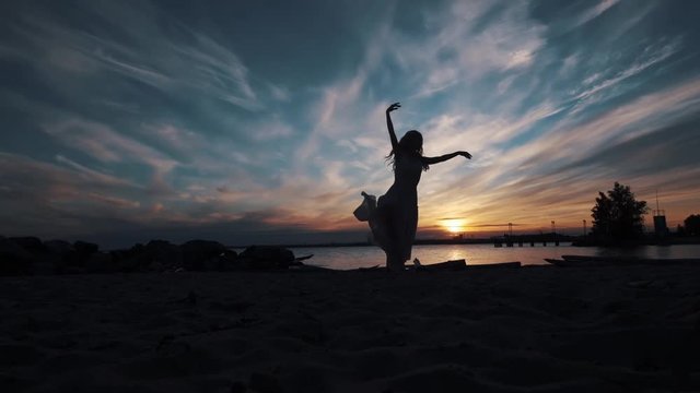 silhouette of a dancing ballerina against the sky at sunset. graceful girl dancing on the seashore.
