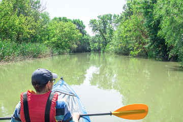 man is paddling on kayak on the river duct, green forest around