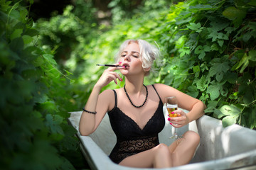 sexy young woman smokes and drinks champagne in a bath in nature