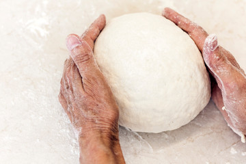 Female hands kneading making dough for dumplings on the table on kitchen.