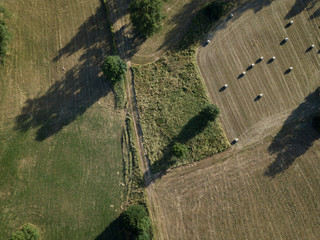 Aerial view of a rural area in Germany in the evening light in Summer. Green and dry fields with long shadows of trees, a few fork-ways and straw bales.