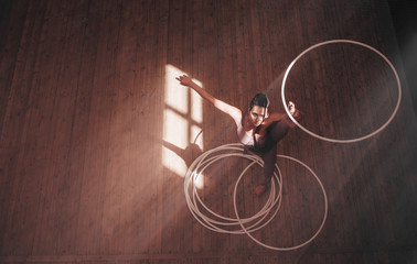 woman performs with several hoops in gymnasium. top view © VlaDee