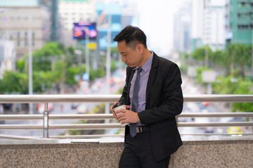 Asian Businessman standing and holding coffee cup with business office buildings in the city background