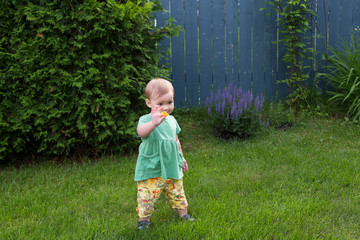 Horizontal full length view of cute fair toddler girl with cheeky expression standing in lawn and holding up a piece of chip