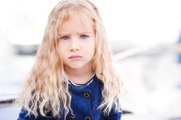 Sad baby girl 4-5 year old with curly blonde hair looking at camera. outdoors.