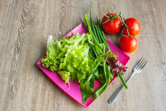 Salad With Greens, Cherry Tomatoes, Onions On Pink Square Plate With Fork On Wooden Table, Overhead View