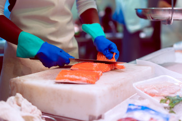 Seller at farmer market in Barcelona cuts salmon for customer. Bright colours, selective focus, bokeh. Barcelona, Spain