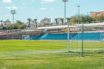 Fototapeta premium common football stadium sport complex building concept photography with gates foreground green grass field and empty tribunes background 