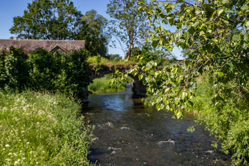 Sunny summer rural landscape with river, old bridge, trees and blue sky.