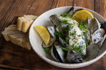 Mussels with sauce and lemon on a wooden table.