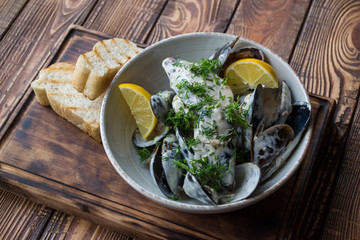 Mussels with sauce and lemon on a wooden table.