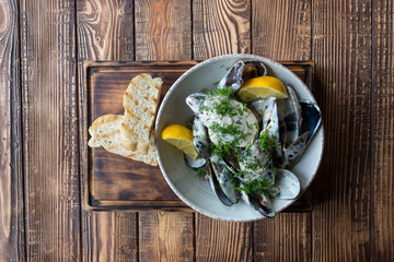 Mussels with sauce and lemon on a wooden table.