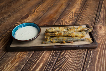 Fried capelin with sause on a wooden table.