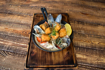 Fried fish with mussels, sauce and lemon on a wooden table.