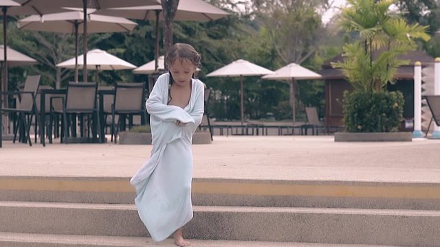 cute tan little girl with wet hair covered in bathe towel goes down stairs from terrace with beach umbrellas slow motion