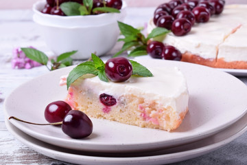 Piece of pie with sour cream and cherries topped with mint on the white plate