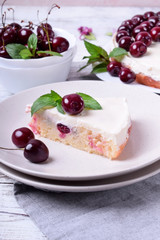 Piece of pie with sour cream and cherries topped with mint on the white plate