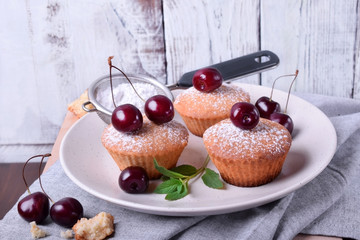 Muffins topped with cherries and sugar powder on the white plate