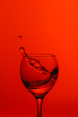 splash of water in wineglass isolated on red background.
