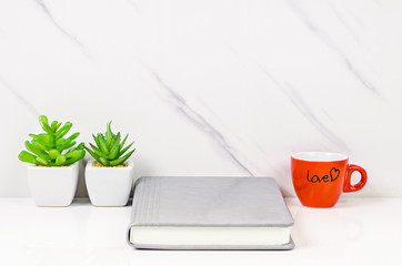 Workspace, notebook and coffee cup with green plant.