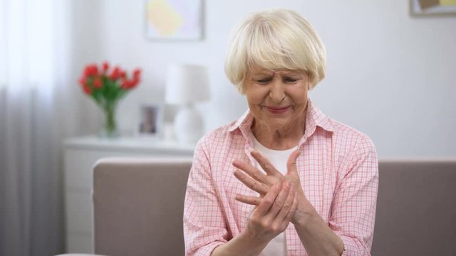 Elderly woman using smartphone, suddenly feeling sharp pain in wrist, arthritis