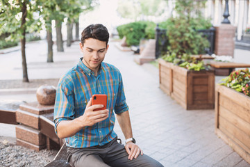 Obraz premium Young handsome business man using smartphone in a city. Cheerful men holding mobile phone. Travel, business, technology concept