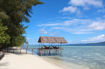 Stilt platform with hammocks over the water on a tropical beach in Raja Ampat on a sunny day.