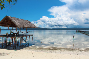 Stilt platform with hammocks over the water on a tropical beach in Raja Ampat on a sunny day.