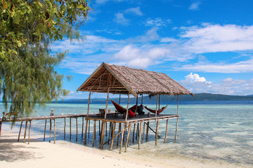 Stilt platform with hammocks over the water on a tropical beach in Raja Ampat on a sunny day.