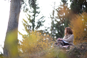 Fototapeta na wymiar A beautiful brunette girl with curls, autumn in the Park by the water reading a book, clothes beige wool large knit, scarf warm, wind blowing, yellow foliage.