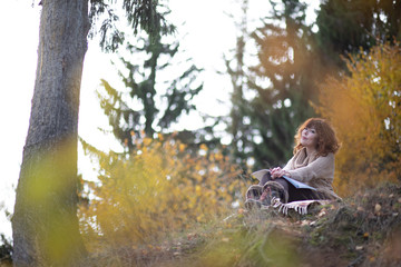 A beautiful brunette girl with curls, autumn in the Park by the water reading a book, clothes beige wool large knit, scarf warm, wind blowing, yellow foliage.