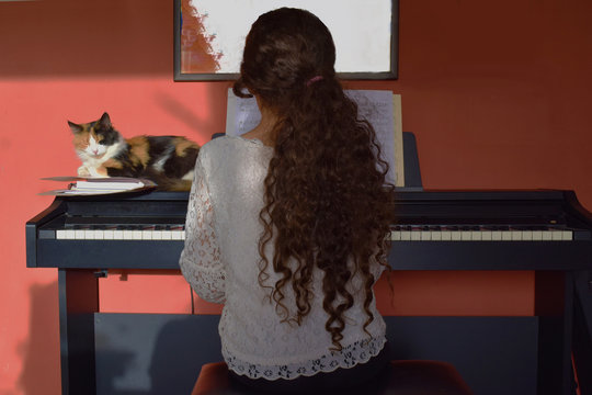 girl pyaying piano in the company of a nice three colors cat