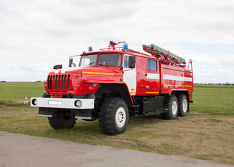 Russian fire truck of red color with retractable ladders stands on the airfield. Summer day, sky with clouds