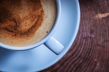 very close up view from above coffee with foam and cinnamon in white ceramic cup on vintage cross section tree trunk