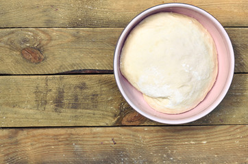 Dough in a pink bowl  on rustic rough wooden table, overhead top view, flat lay, closeup, copy space, homemade cooking and pastery concept