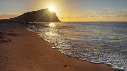 Dramatic sunrise over Montana Roja an unusual, stratovolcanic cone and La Tejita beach, one of the longest, natural beaches in Tenerife, Canary Islands, Spain. Panoramic perspective with natural light