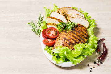 Grilled chicken breasts with salad leaves tomatoes and herbs on white dish. Selective focus, space for text.