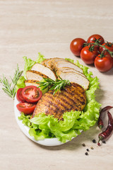 Grilled chicken breasts with salad leaves tomatoes and herbs on white dish. Selective focus, space for text.