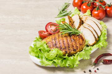 Grilled chicken breasts with salad leaves tomatoes and herbs on white dish. Selective focus, space for text.