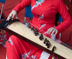 a woman dressed in traditional red with bird motif plays a Dann Tranh (đàn thập lục) This is...