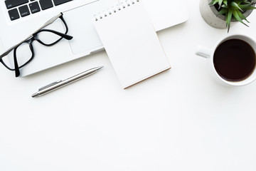 Small blank notebook is on top laptop computer on white office desk table with cup of coffee, pen and supplies. Top view with copy space, flat lay.