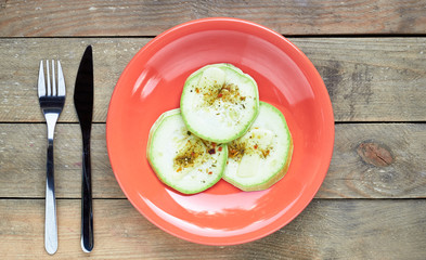 Roasted zucchini with spices in a living coral plate served on wooden rustic table, flat lay, overhead top view, closeup, copy space, vegetarian food concept
