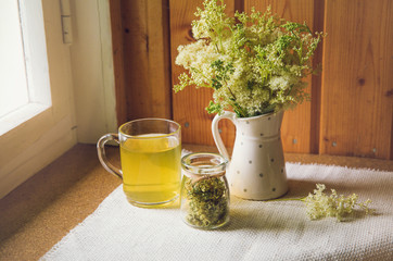 Fresh Meadowsweet, Filipendula ulmaria in jug shape vase and it`s herbal tea in glass, tea powder in jar. Indoors country home house.