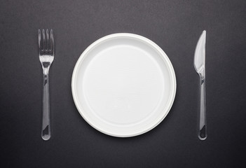 Plastic disposable tableware. Plate, fork and knife on black background, top view